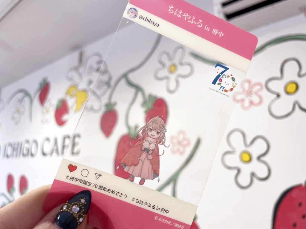 「ちはやふる in 府中」のクリアカードが「ICHIGO CAFE」の店内で撮影された写真。背景にはいちごと花の可愛らしいイラストが描かれています。カードにはキャラクター「千早」が描かれ、SNS風のフレームと府中市70周年のロゴも見られます。イベントやコラボカフェの記念として提供されているアイテムです。