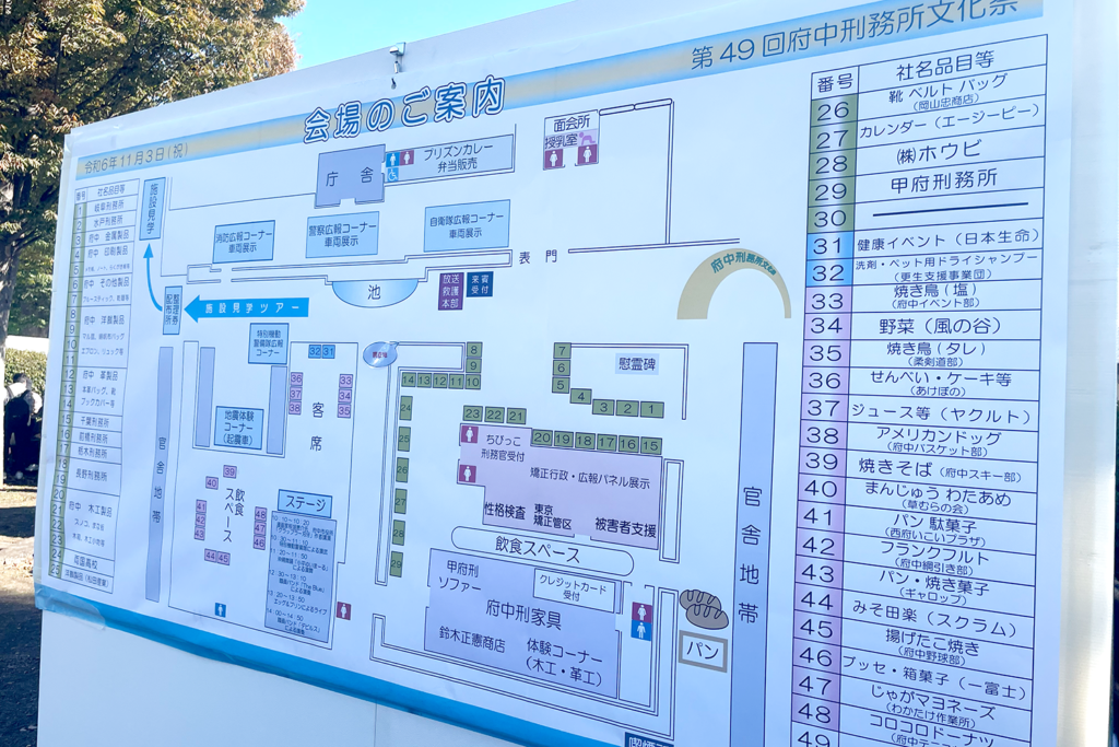 第49回府中刑務所文化祭の会場案内図です。地図には各エリアや出展ブースが細かく記載され、矯正展の位置、飲食スペース、ステージ、体験コーナーなどの詳細が示されています。右側にはブースごとの出展内容がリスト化されており、食品販売や工芸品展示などが含まれています。地図の背景には会場の一部と木々が見え、屋外イベントの様子が伝わります。