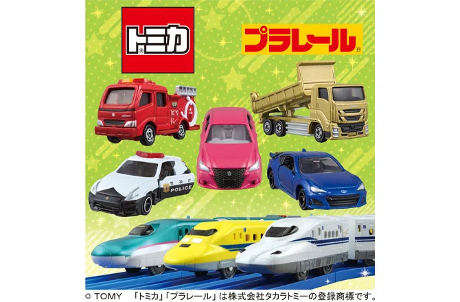 トミカとプラレールの車両と新幹線のおもちゃが並んでいるイメージ。緑色の背景にカラフルな車両（消防車、パトカー、スポーツカー、ダンプトラック）と、新幹線（はやぶさ、こまち、のぞみ）などが描かれています。