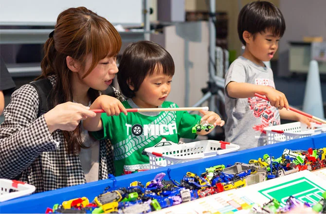 トミカの遊び場で車のおもちゃを楽しむ親子の様子。母親と子どもが釣りゲームのようにおもちゃを取り出している場面。