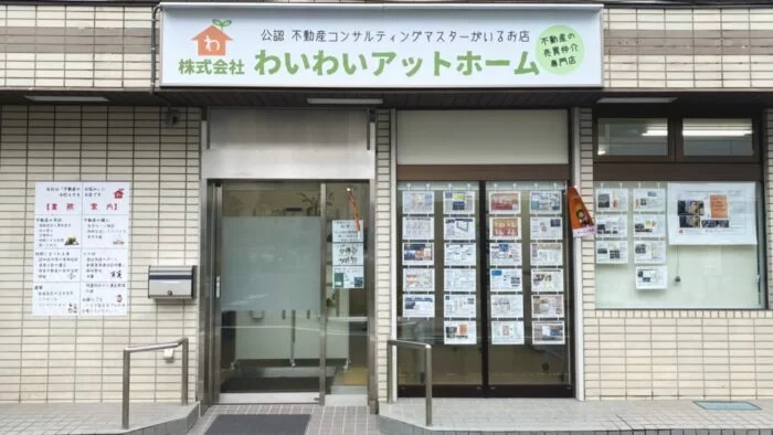 東京都府中市にある不動産会社「株式会社わいわいアットホーム」の店舗外観。看板には「公認 不動産コンサルティングマスターがいるお店」と記載され、窓ガラスには物件情報が多数掲示されている。