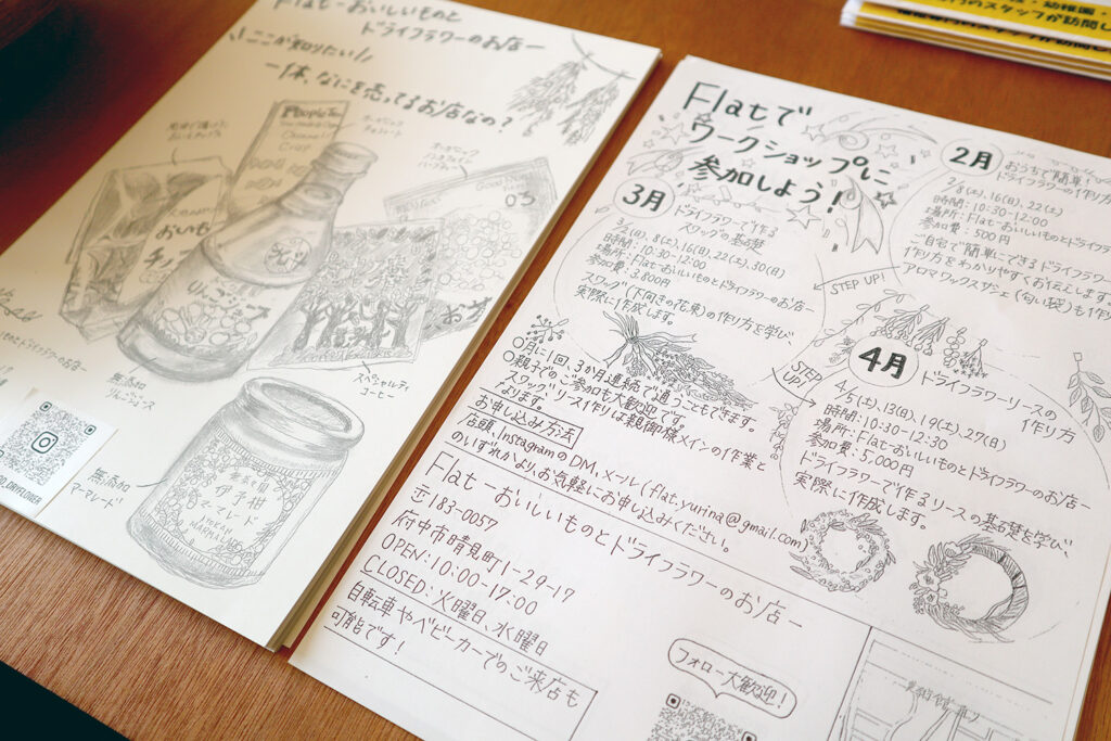 手描きイラスト入りのチラシがテーブルに置かれており、「Flatでワークショップに参加しよう!」と題した案内が記載され、ドライフラワーリースの作り方や店舗情報が紹介されている。